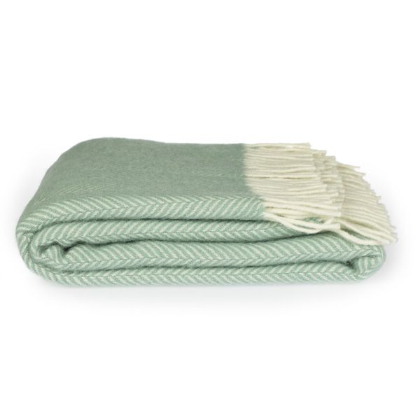 Side view of a folded seafoam green fishbone throw, with cream tassels on the right side.