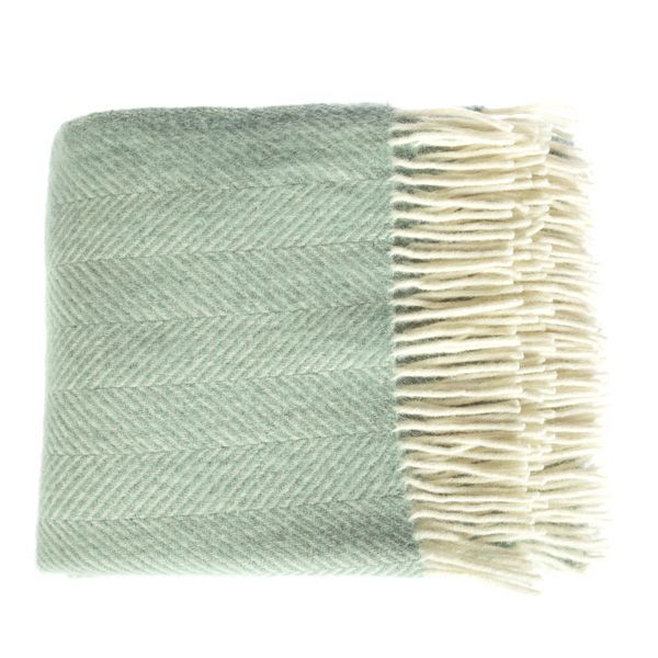 Top down view of a folded seafoam green fishbone throw, with cream tassels on the right side.