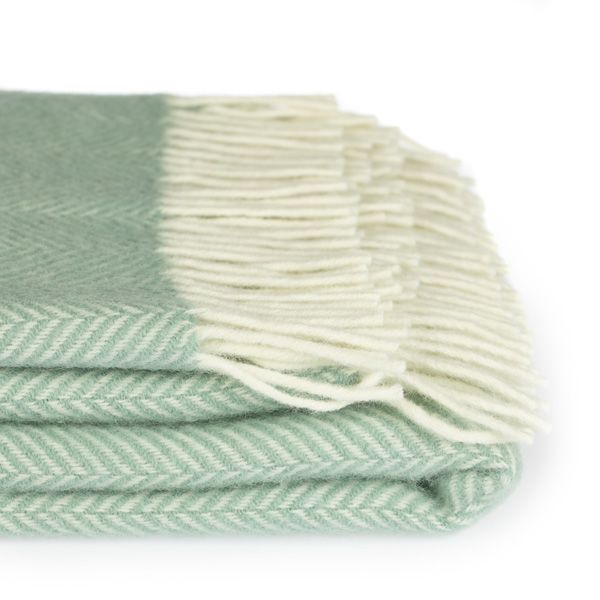 close up on the detail on the folded seafoam green fishbone throw, with cream tassels on the right side.