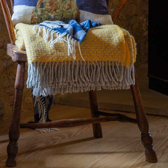 The Yellow Twill Wool Throw folded up hanging down over a wooden armchair.