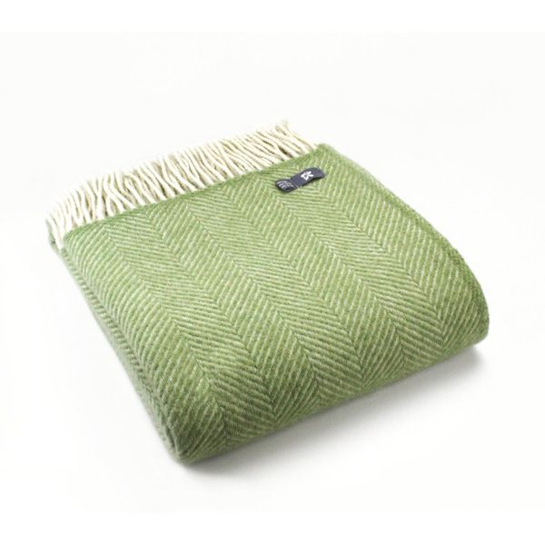 Three quarter view of the Fern Green Fishbone Throw folded up, with cream tassels to the top side.