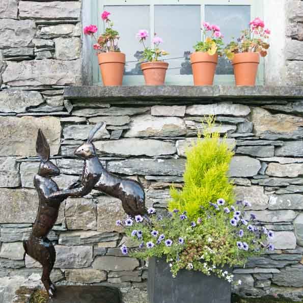 The boxing hares sculpture in a garden against a wall to show the product in situ.