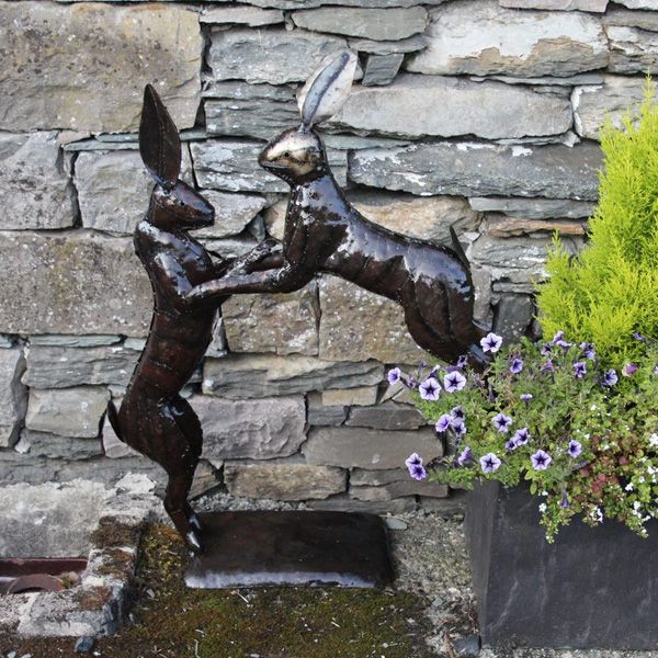 A close up of the boxing hares sculpture in a garden against a wall to show the product in situ.