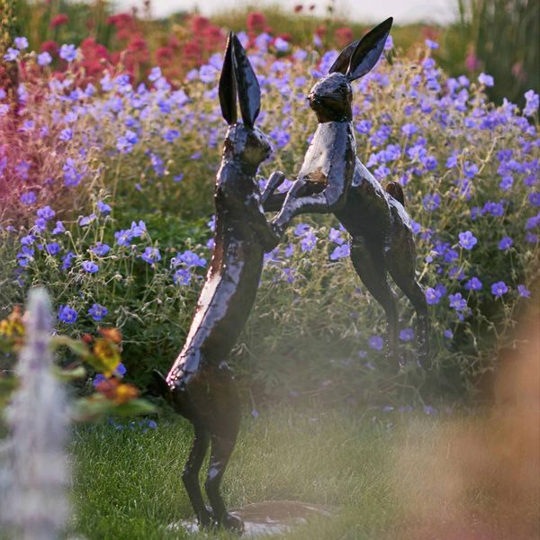 The boxing hares sculpture in a garden full of flowers to show the product in situ.
