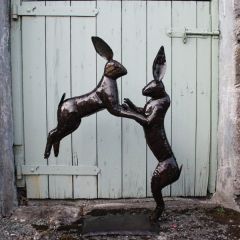 Sculpture of two boxing hares, one is standing on the ground and the other in the air. They are connected by their arms in a boxing stance.