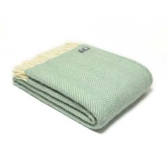 Three quarter view of a folded seafoam green fishbone throw, with cream tassels on the left side.