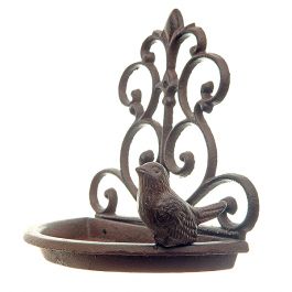 A cast iron wall mounted bird feeder with scroll detailing and a small bird perched on the edge of a semi circular dish