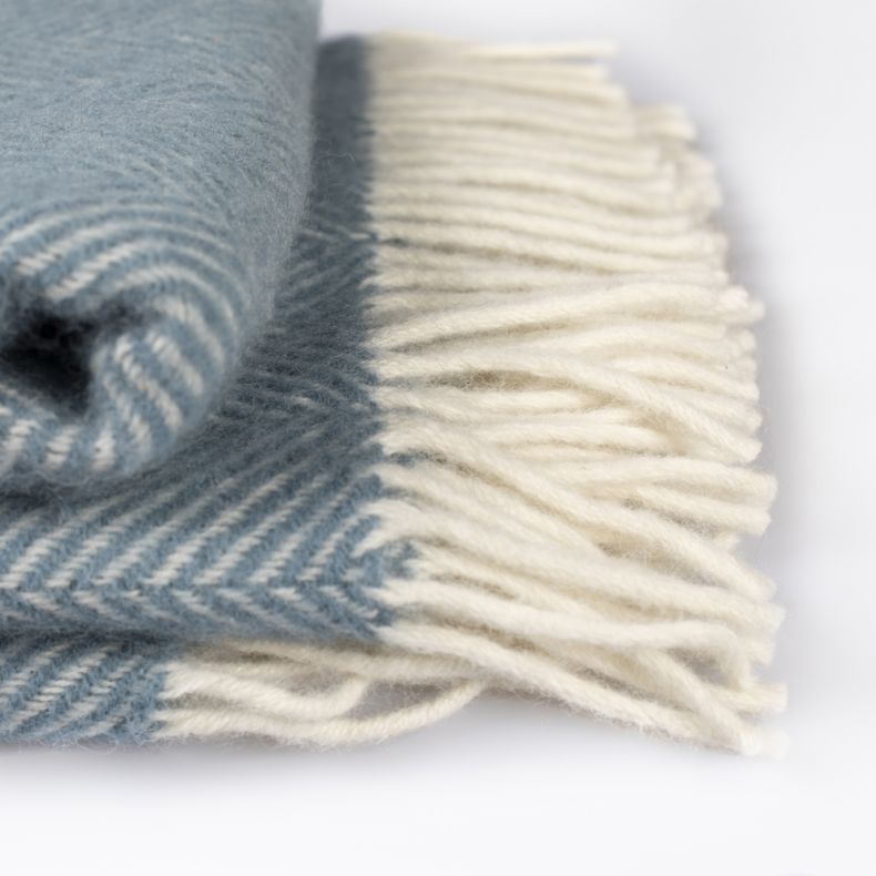 Close up of the Petrol Blue Herringbone Wool Throw folded up, with cream tassels to the right.