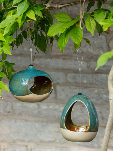 Wildlife care - browse the National Trust shop for bird baths, feeders and wildlife care designed with nature in mind. This image shows the CJ Wildlife Drinker and CJ Wildlife Feeder, hanging from a tree branch surrounded by foliage.