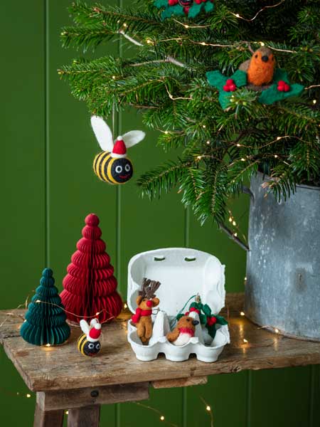 National Trust Christmas decorations range, from baubles and tree toppers to paper garlands, hanging decorations and advent candles. Image shows felt decorations on a real Christmas tree, with our bestselling Set of 6 Festive Woodland Characters in Egg Box on nearby bench. Browse the range for decs, gifts and more inspired by National Trust places - every purchase helps look after nature, beauty and history.