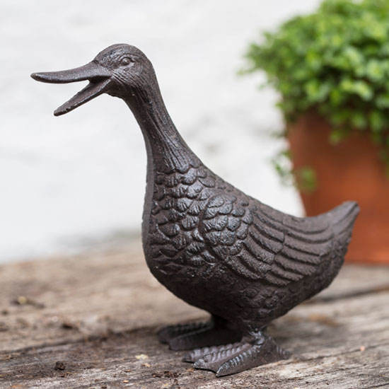 Cast Iron Duck. Image shows cast iron garden ornament displayed on a garden table with a terracotta garden pot and potted herbs in the background.