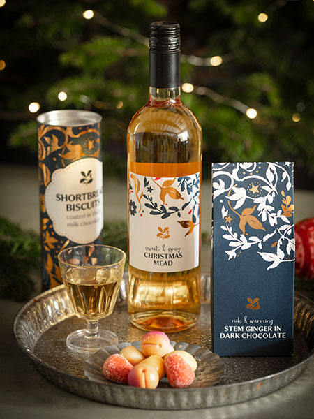 Festive food - image shows the Christmas Mead, Stem Ginger in Dark Chocolate and Shortbread Biscuits from the National Trust's Christmas food range arranged on an antique style silver platter with the glow of Christmas lights in the background.