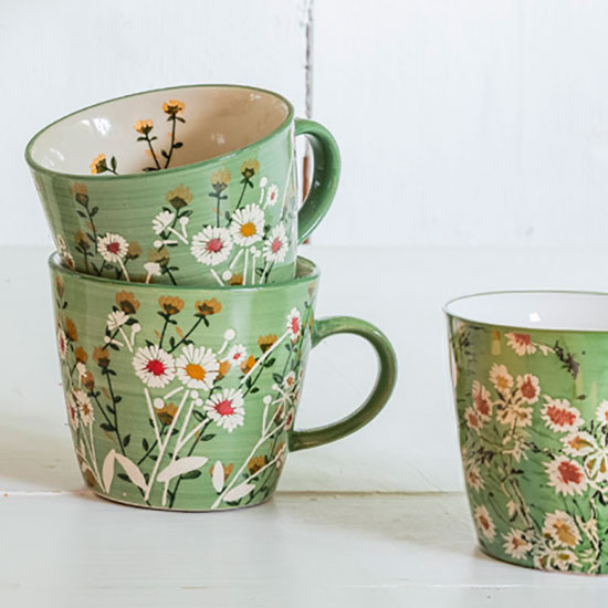 Ceramic Mug - Green Wild Daisy. Image shows three ceramic Wild Daisy Mugs, decorated with a green background and painted white daisies, stacked on a side board ready for making the perfect cup of tea.