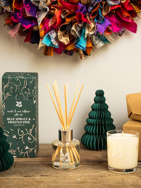 Hampers & gift sets - image shows the Blue Spruce and Frosted Pine Reed Diffuser and Candle Gift Set on a sideboard, surrounded by festive decorations including the Recycled Sari Wreath.