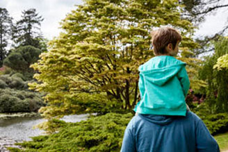 Gift membership - celebrate a birthday, anniversary or special moment with a gift membership from the National Trust. Image shows adult and child exploring the outdoors together, with trees and foliage in the background.  
