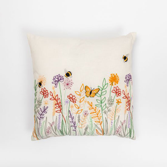 Bees and Blossom Embroidered Cushion - £25.00, from the National Trust's new homeware range. Image shows square cushion with bee and flower motifs in bright colours, laid on a plain grey background.
