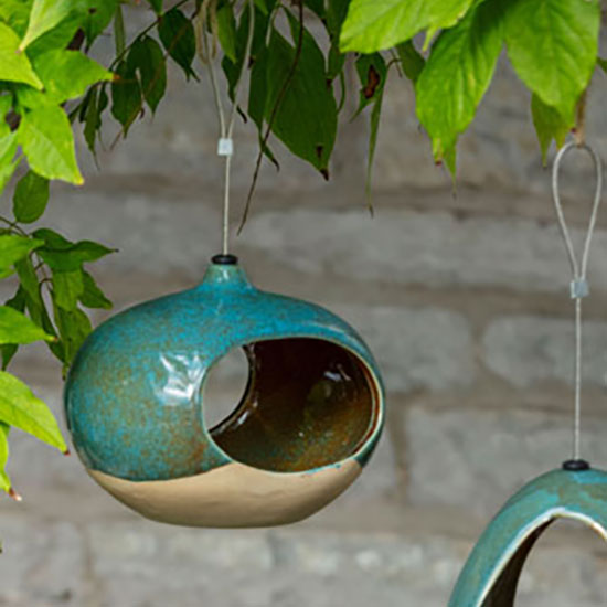 CJ Wildlife Vierno Seed Feeder (£10.00) - from the bird and wildlife care range. Image shows seed feeder hanging from a tree, in amongst foliage. Every purchase helps look after the places in our care for everyone, for ever.