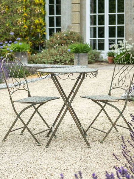 Garden furniture. Image shows Avalon Bistro Set with two folding chairs and circular table in a country house garden setting, with greenery and foliage in the background.