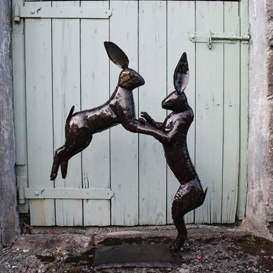 Large Boxing Hares Garden Sculpture (£110). Image shows metal boxing hares sculpture, with one stood and one leaping, on a garden patio.