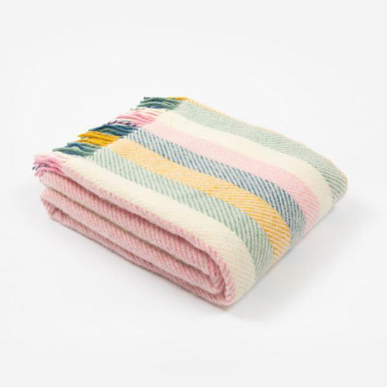 National Trust Wool Blanket, Coastal Sunset (£48.00) - image shows wool throw with stripes in the colours pink, yellow, blue and green. Throw has corresponding coloured tassels and is shown folded on a plain grey background. Browse the throws and blankets range for homeware that helps look after National Trust places for everyone, for ever.