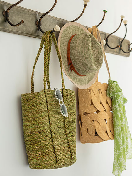 Fashion accessories. Image shows a range of bags, including the green Seagrass with Handles and Jute Basket Bag, hanging in a hallway on antique hooks.
