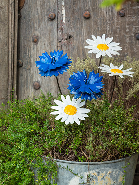New in - browse the National Trust shop for find unique and unusual garden decor, fashion, homeware and more. This image shows the Cornflower Plant Stake and Daisy Plant Stake, available as packs of two, in a metal planter surrounded by green foliage. Made from recycled metal, these plant stakes are both decorative and functional - give your plants a helping hand, while brightening up your outdoor space.