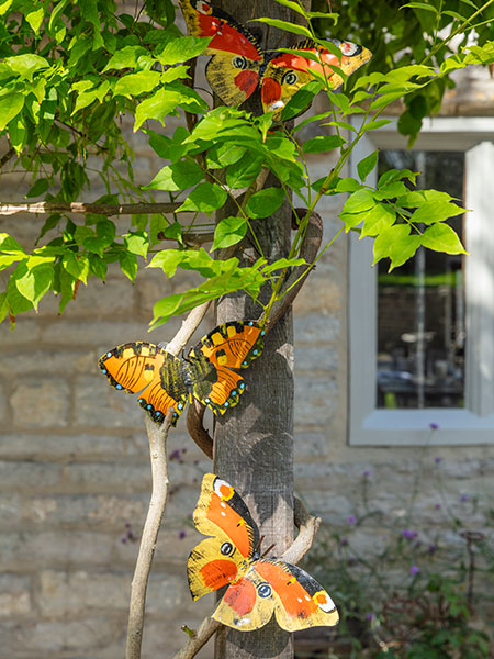 Garden decor. Image shows three Butterfly Sculptures fixed against a garden pergola, as if flying in and through the nearby foliage. 