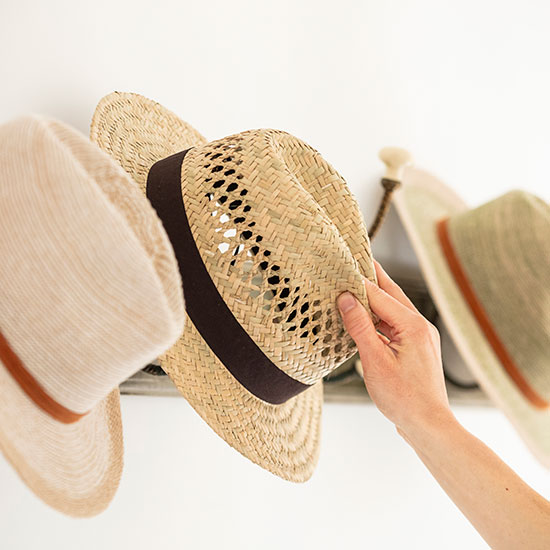 National Trust Straw Hat (£22.00). Image shows model reaching to retrieve hat from hook.