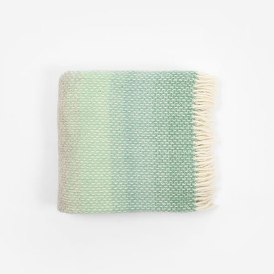 National Trust Throw - Ombre Green (£48.00). Image shows ombre green throw folded on a plain grey background. Ombre starts from a deep sea green to lighter fern green, into grey with cream tasselling.