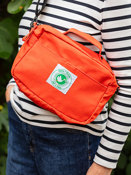 Outdoor accessories - browse the National Trust outdoor accessories range for great gifts and useful accessories designed for exploring nature. Image shows model wearing new Utility Bag in orange, made by Cora & Spink.