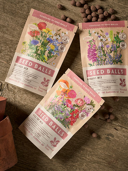 New in. Image shows seed ball packs, designed in collaboration between National Trust and Blue Diamond, laid out on a garden workbench. Each seed pack is inspired by a National Trust place - from Sizergh to Nymans.