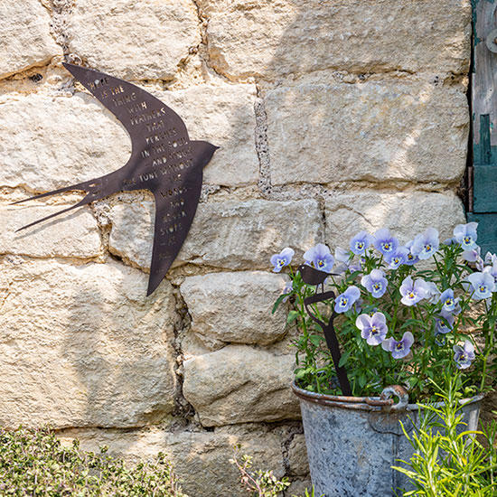 Swallow Wall Art - £40.00, from the National Trust's garden decor range. Image shows wall art shaped like a swallow, with poetry by Emily Dickinson, against a stone garden wall. Made with weatherproof steel, browse the new garden decor range at the National Trust's online shop for this garden sculpture and more garden wall art. Help care for nature, beauty and history for everyone, for ever.