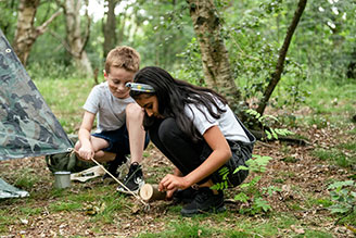 Childrens activity & craft kits - image shows two children playing with The Original Den Making Kit, surrounded by nature. Both are contructing an awning using the tools provided by the Den Kit.