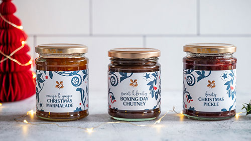 National Trust food & drink - image shows three festive treats from our Christmas food range arranged on a kitchen work surface, including the Christmas Pickle, Marmalade & Boxing Day Chutney.  