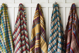 Outdoor rugs & picnic blankets - image shows several Recycled Rugs from the National Trust outdoor range hung on hooks in a hallway, ready to pack into a rucksack and explore the outdoors. 