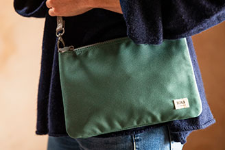 Bags - image shows ROKA Cross Body Bag in Sage worn by a model, wearing a dark navy sweater.