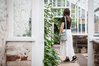 Bags - image shows ROKA Cross Body Bag in Sage worn by a model, wearing a dark navy sweater.